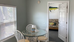 A dining area with a glass table and white chairs, a ceiling fan, and a door leading to another room. - OCEANSIDE BEACH HOUSE-3 BED/2 BATH. GOLF-CART INCLUDED, 100 YARDS FROM BEACH (Myrtle Beach)