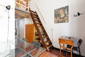 A room with a glass table, chairs, a wooden desk, a ladder, and a painting on the wall. - GuestHost - Milan Cadore - Urban Retreat Apartment! (Milano)
