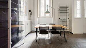 Una habitación con una mesa, sillas, un radiador, una ventana y una estantería.