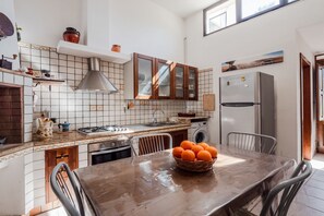 Una cocina con salpicadero de azulejos, armarios de madera, un refrigerador de acero inoxidable y una mesa de comedor con un cesto de naranjas.