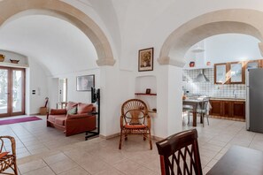 Un área de sala y comedor integrada, con sofá, mesa de comedor, sillas y una cocina visible a través de un arco.