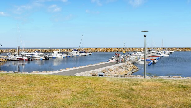 En småbåtshamn med förtöjda båtar, en vågbrytare av sten och en klar himmel.