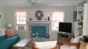 A living room with teal and white furniture, a fireplace, and a television. - Cape Cottage with 5 beds, large deck, and less than 10 minute walk to the beach! (Eastham)