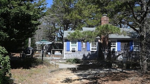 A house with a chimney, blue shutters, and a covered outdoor area. - Cape Cottage with 5 beds, large deck, and less than 10 minute walk to the beach! (Eastham)