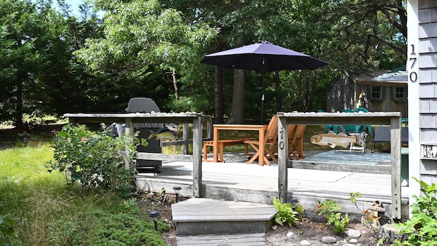 A wooden deck with outdoor furniture, a table, and a chair. - Cape Cottage with 5 beds, large deck, and less than 10 minute walk to the beach! (Eastham)