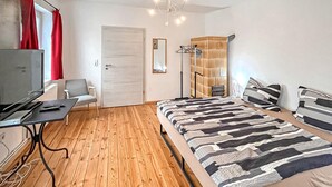 A modern bedroom with a wooden floor, a bed with striped bedding, a desk with a TV, and a wardrobe with a mirror.