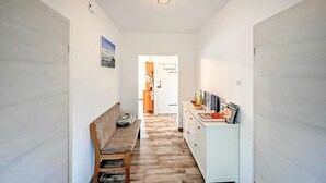 A hallway with a bench, a cabinet with books and decorative items, and a door leading to another room.