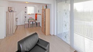 Een woonkamer met een leren bank, een houten kast, een eettafel met stoelen en een raam met jaloezieën.