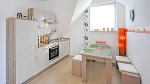 Een compacte keuken met witte kasten, een inbouwoven en een kleine eettafel met een broodtrommel.