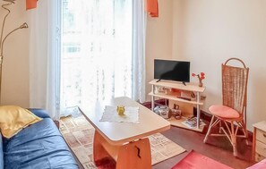 Una sala de estar acogedora con un sofá, una mesa de centro, un televisor sobre un mueble y un sillón de mimbre.