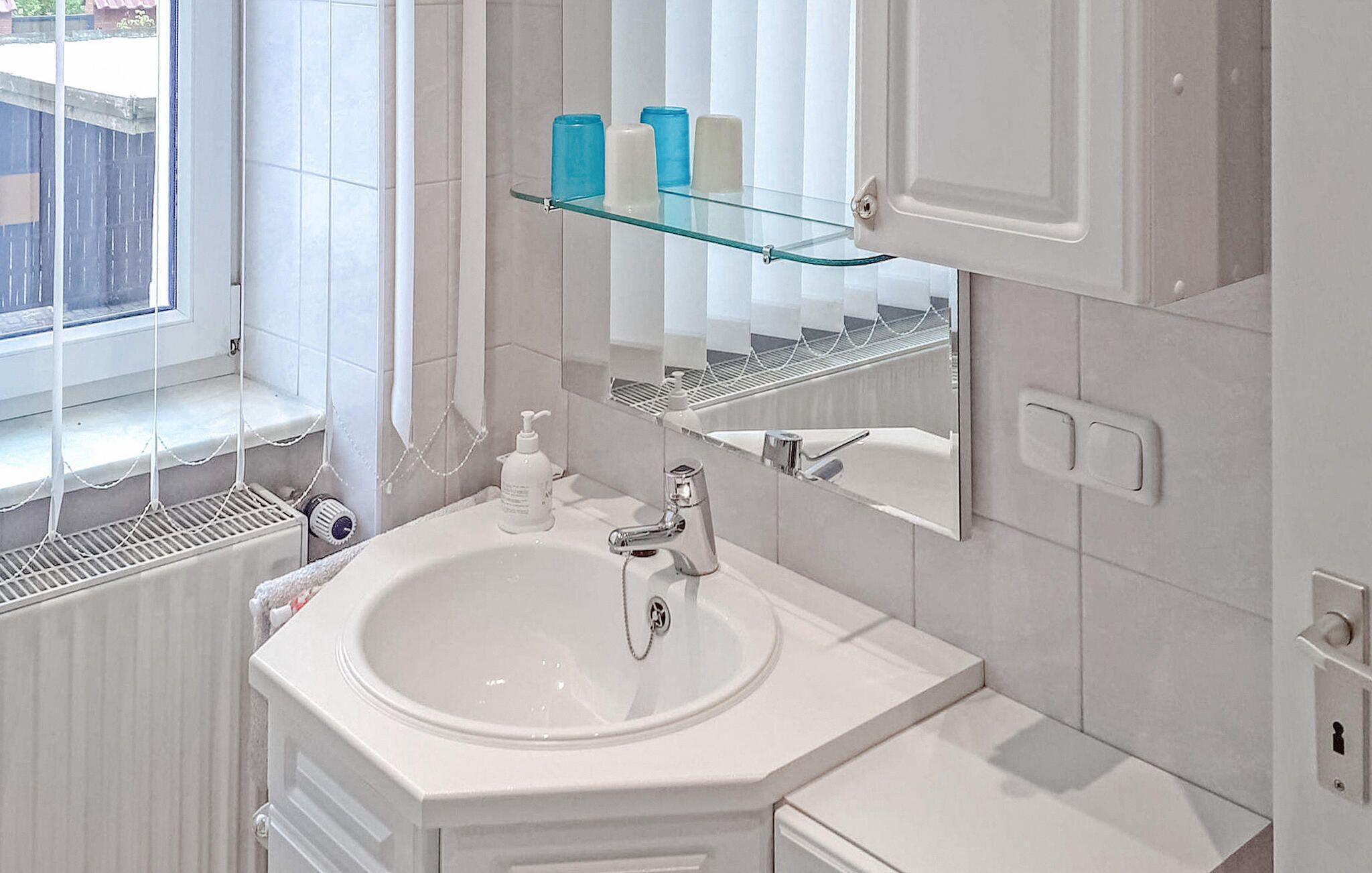 A bathroom with a white sink, a mirror, and a glass shelf above it.