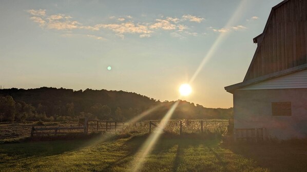 A barn with a fence in a rural setting during sunset.