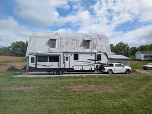 A large RV parked in front of a house with a metal roof.
