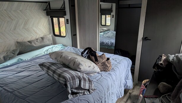 A bedroom with a bed, pillows, a bag, and a door leading to another room.