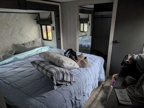 A bedroom with a bed, pillows, a bag, and a door leading to another room.