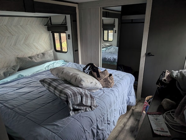 A bedroom with a bed, pillows, a bag, and a door leading to another room.