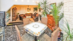 Un comedor con piso de mármol, sillas de mimbre, una mesa con mantel floreado y plantas en macetas.