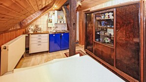 Un dormitorio acogedor en el ático, con techo inclinado, vigas de madera, una cama blanca, un armario azul y un guardarropa de madera.