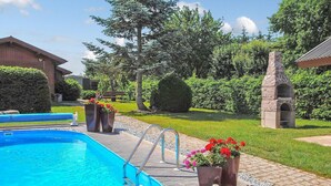 A swimming pool with a metal ladder, surrounded by a brick pathway, potted plants, and a stone structure. - Stunning home in Kummerow with sauna (Kummerow)