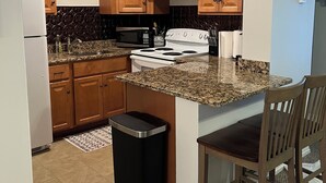 A compact kitchen with wooden cabinets, a stove, a microwave, and a trash bin. - Lake Winnipesaukee, Weirs Beach! (Laconia)
