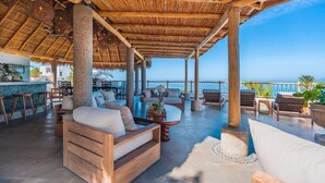 A covered outdoor lounge area with wooden furniture, a pool, and a view of the ocean. - Las Villas Puerto Vallarta (Puerto Vallarta)