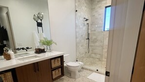 A modern bathroom with a glass-enclosed shower, a white toilet, and a vanity with a mirror and toiletries. - Luxurious King Suite in Gilbert. Kids are Welcome! (Gilbet)