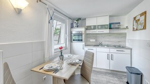 A compact kitchen with white cabinets, a built-in oven, and a dining area with a wooden table and chairs.