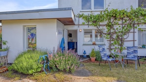 A two-story house with a small attached garage, a garden with various plants and a blue chair, and a visible door to the garage.