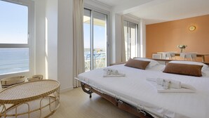 A hotel room with a large bed, a balcony with a view of the sea, and a wicker chair. - Appartement Victoire, vue mer - Welkeys (Biarritz)