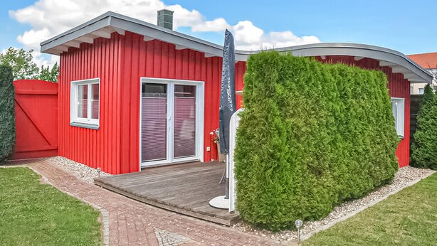 Ein rotes Gebäude mit einer Holzterrasse, einer überdachten Veranda und einer gepflegten Hecke.