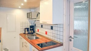Eine kompakte Küche mit einer Holz Arbeitsplatte, einer eingebauten Spüle und einer Mikrowelle darüber. Es gibt weiße Schränke mit silbernen Griffen und eine geflieste Spritzschutzleiste mit roten und blauen Akzenten.