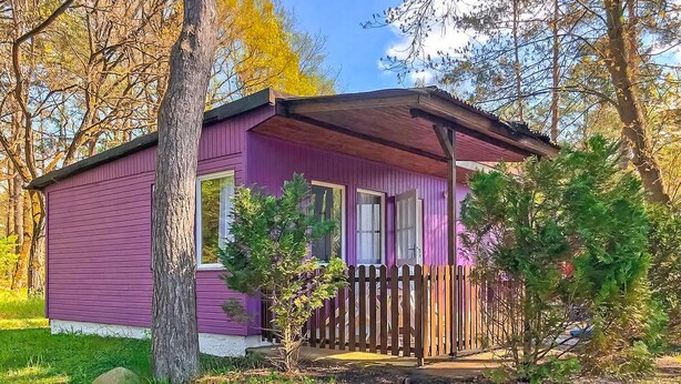 Une petite cabane d’un seul étage, à l’extérieur violet, avec un porche en bois et une cour clôturée.