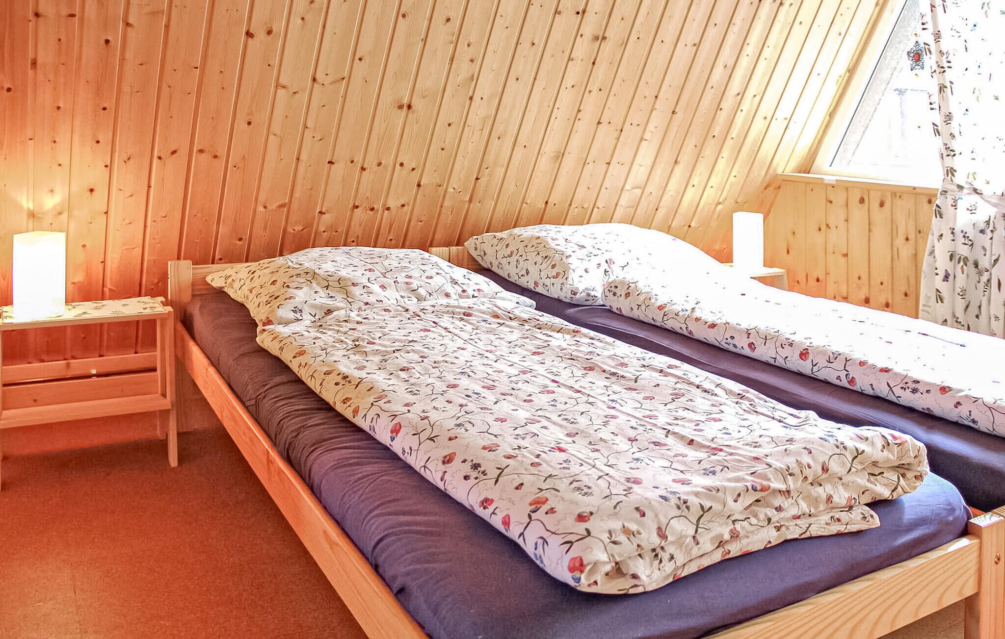 A cozy wooden room with two beds, a nightstand, and a window with curtains.