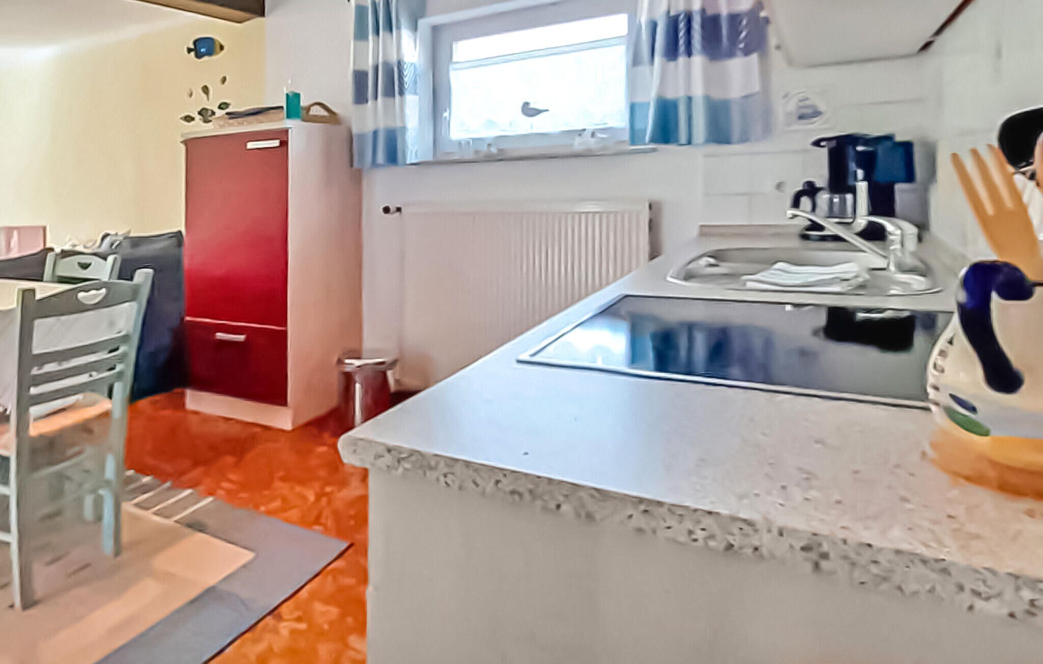 A compact kitchen with a red cabinet, a white countertop, and a window with curtains.
