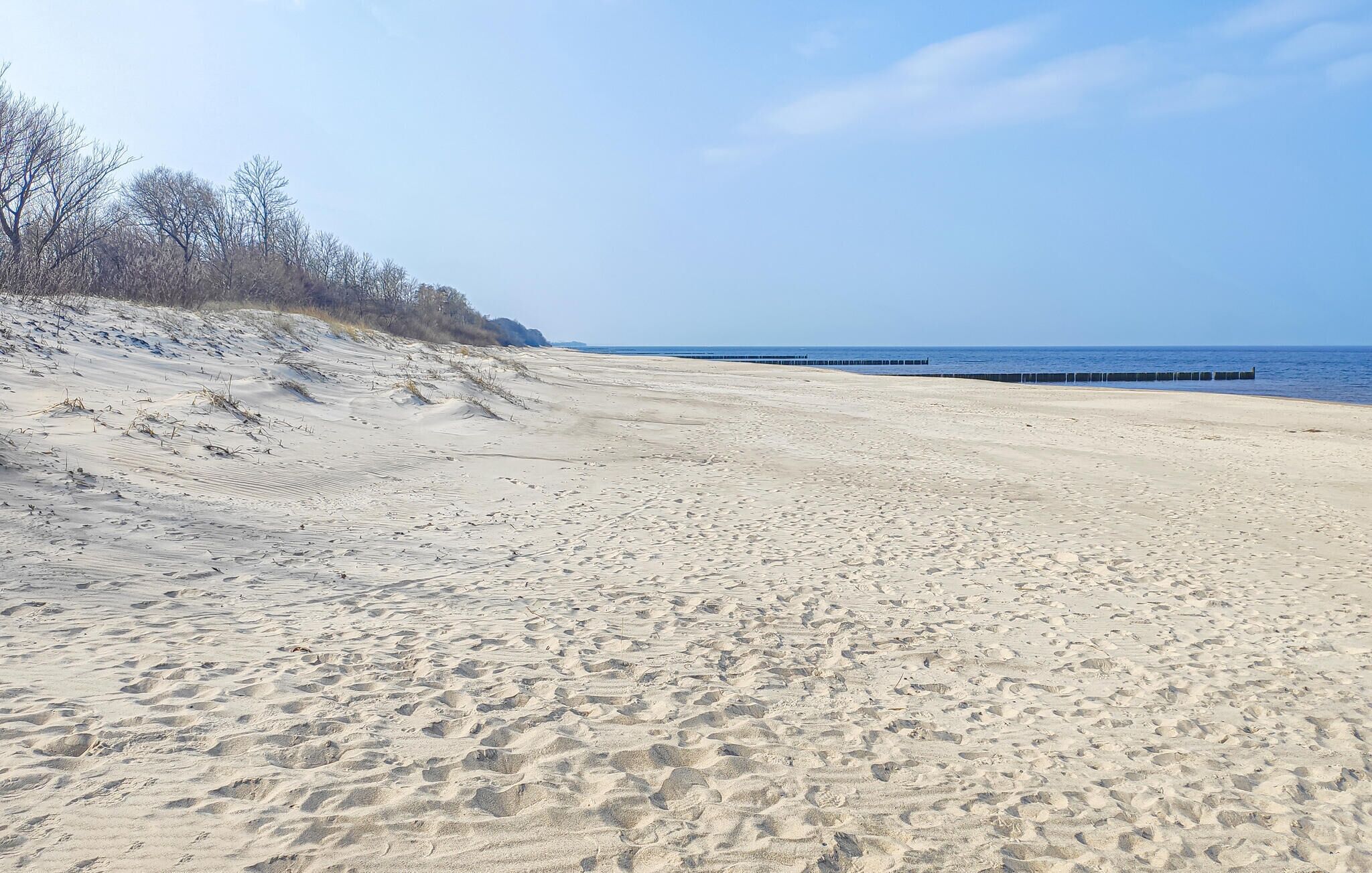 Een zandstrand met een heldere lucht en een pier in de verte.