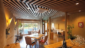 A restaurant with wooden tables and chairs, a bar area with wine bottles, and a view of the outdoors through large windows. - WAIN TO OYADO CHITOSE (Miyazu)