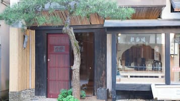 A building with a red door, a small tree in front, and a window displaying items inside.