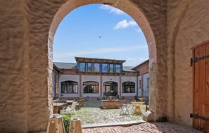 Ein Innenhof mit Steinpflaster, einer Holztür und einem Gebäude mit Rundbogenfenstern und einem Ziegeldach.