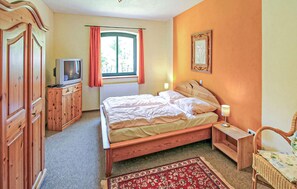 Ein Schlafzimmer mit einem Bett, einem Fernseher, Holzmöbeln, einem Fenster mit Vorhängen und einem gerahmten Bild an der Wand.