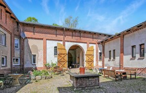 Ein Innenhof mit Backsteingebäuden, einem zentralen Bogen, Außenplätzen und einem kleinen Brunnen.