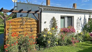Un piccolo edificio bianco con un cancello in legno, circondato da fiori colorati e un giardino.