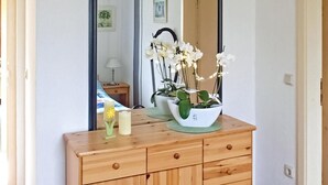 Un comò in legno con cassetti, uno specchio e una pianta in vaso con fiori bianchi.