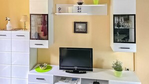 Un soggiorno moderno con televisione a schermo piatto, mobili bianchi e oggetti decorativi sugli scaffali.