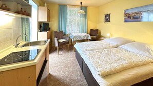A compact hotel room with a kitchenette, a bed with white bedding, a small table with a chair, and a window with curtains. - Ferienwohnung Zinnowitz Seebad (Zinnowitz (Seebad))