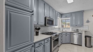 Una cocina moderna con armarios grises, electrodomésticos de acero inoxidable y salpicadero de azulejos.