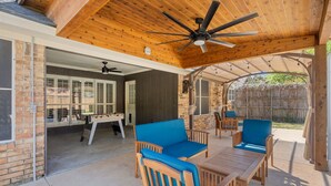 Un patio al aire libre con mobiliario de madera, un ventilador de techo y una pared de ladrillo.