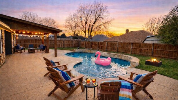 Un patio trasero con piscina, sillas de descanso, un bar tiki y un pozo de fuego.