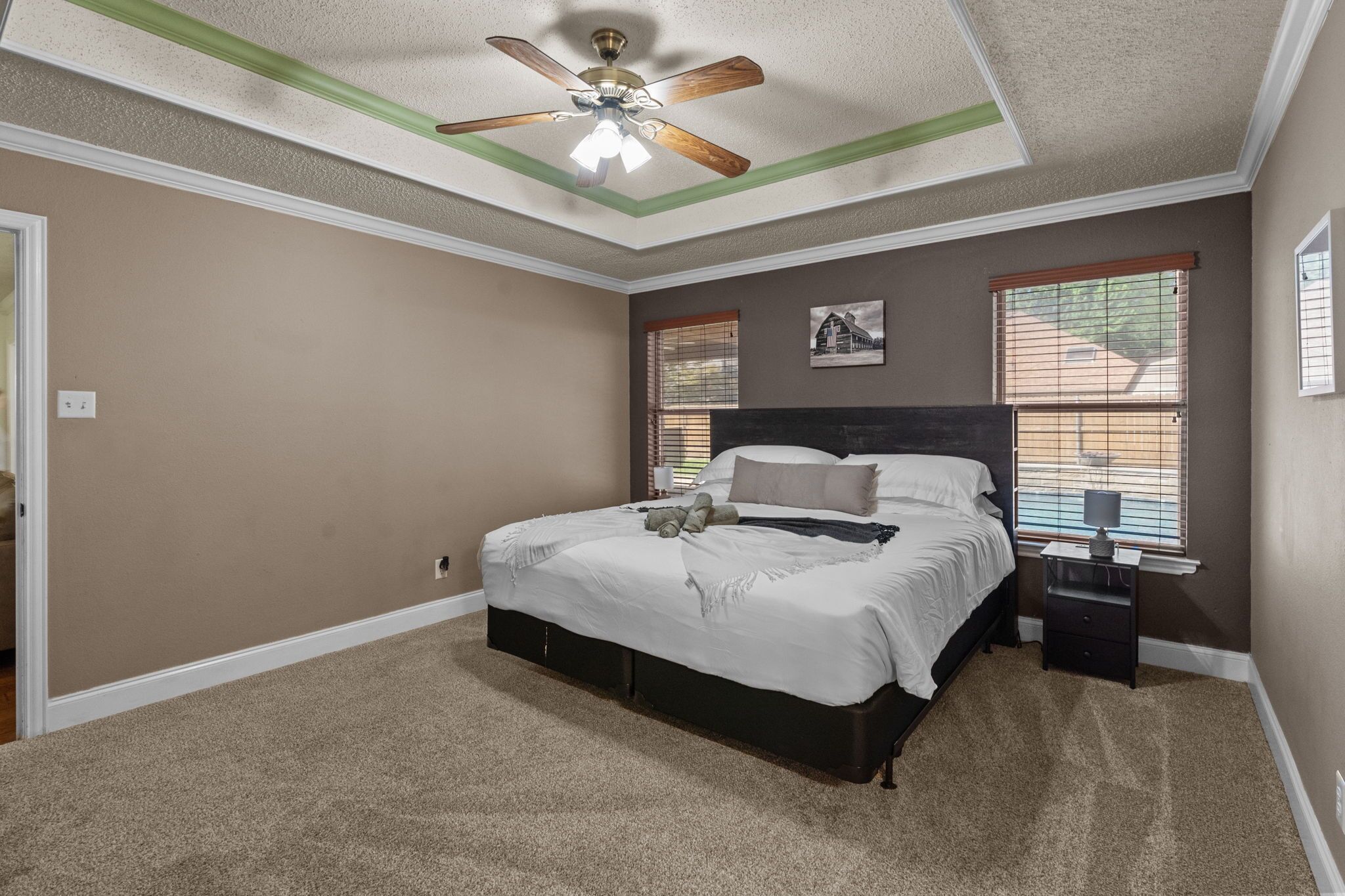 A bedroom with a bed, a nightstand, a ceiling fan, and two windows with blinds.