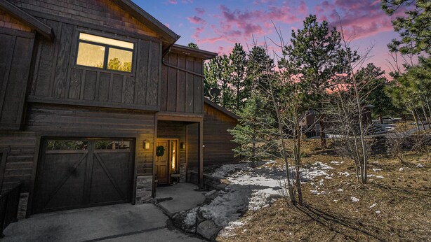 A two-story wooden house with a garage, a front door, and a small porch. - Estes Park Luxury Family Retreat- EV Charger/Hot Tub/Game Room/Outdoor Fire Pit (Estes Park)