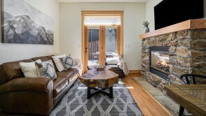 A cozy living room with a stone fireplace, a brown leather sofa, and a ceiling fan. - Estes Park Luxury Family Retreat- EV Charger/Hot Tub/Game Room/Outdoor Fire Pit (Estes Park)